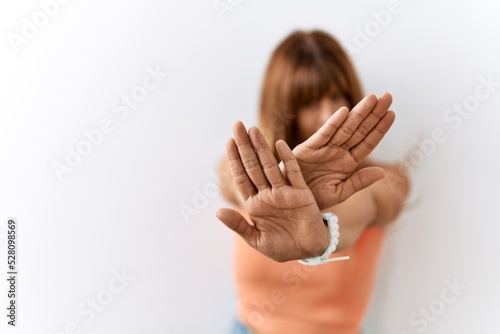 Hispanic woman with bang hairstyle standing over isolated background rejection expression crossing arms and palms doing negative sign, angry face