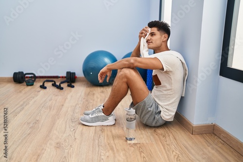 Young hispanic man tired relaxed sitting on floor at sport center