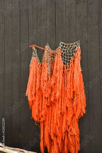 Oudeschild, Netherlands. August 2022. An orange fishing net against a black tarred wooden wall on Texel.