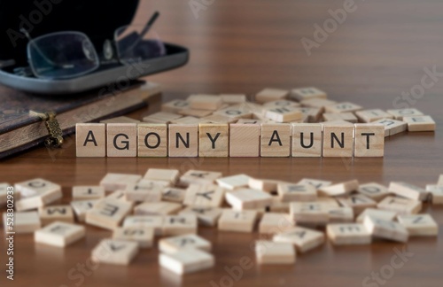 agony aunt word or concept represented by wooden letter tiles on a wooden table with glasses and a book
