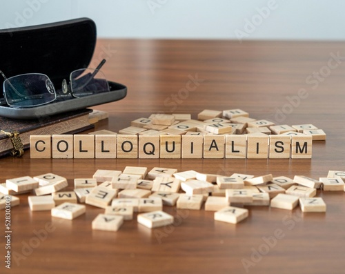 colloquialism word or concept represented by wooden letter tiles on a wooden table with glasses and a book