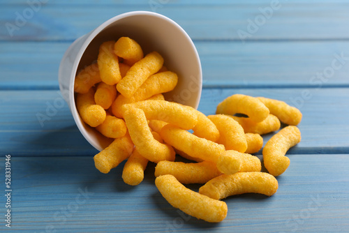 Many tasty cheesy corn puffs on blue wooden table