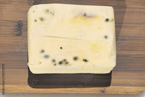 a pack of spoiled butter with mold on a wooden board