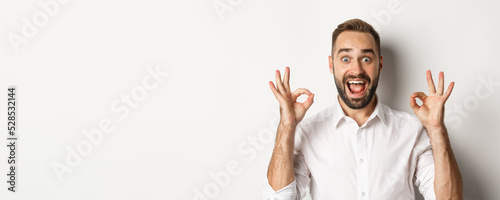 Close-up of amazed caucasian guy agreeing, showing okay signs and looking impressed, recommending product, white background