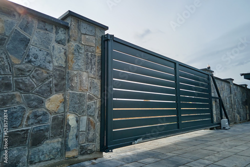 Wide automatic sliding gate with remote control installed in high stone fense wall. Security and protection concept