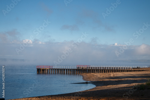 View of the beach with concrete piers and dissipating fog over the river in the early morning.