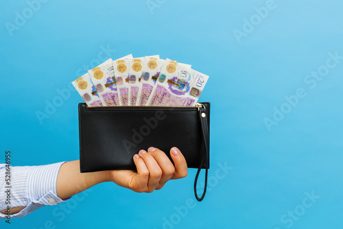 Female hands holding british pounds banknotes in black wallet on a blue background.
