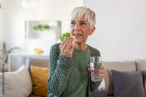 Senior woman takes pill with glass of water in hand.