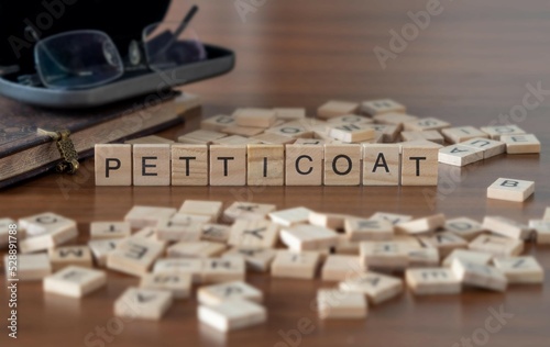 petticoat word or concept represented by wooden letter tiles on a wooden table with glasses and a book