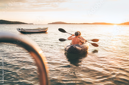 Two rowers on inflatable kayak rowing by the evening sunset rays Adriatic sea harbor in Croatia near Sibenik city. Vacation, sports, and a recreation concept image.