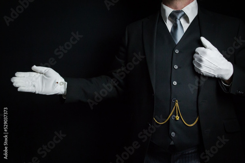 Portrait of Butler in Dark Suit and White Gloves Standing With Welcoming Gesture. Concept of Service Industry and Professional Hospitality.