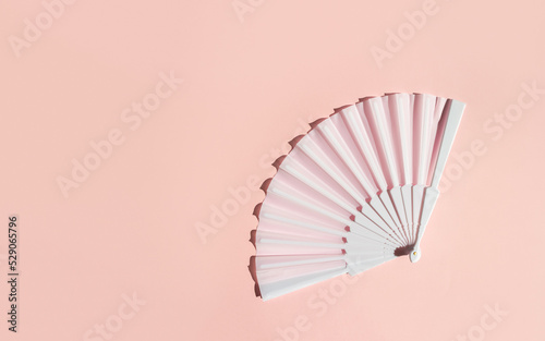 White fan on a pastel background. Minimal creative concept of menopause and female hot flashes. Copy space, flat lay