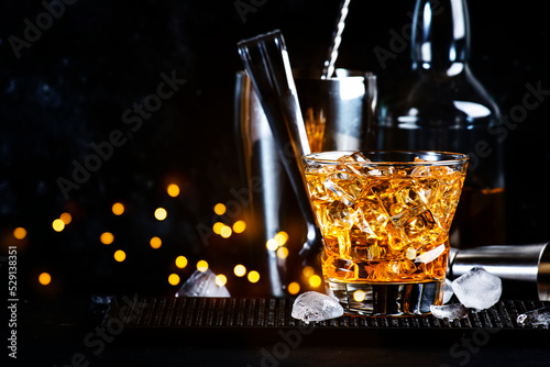 Godfather cocktail with scotch whiskey, almond amaretto liqueur and ice cubes.. Black background, steel bar tools