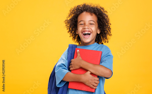 Happy ethnic schoolboy laughing with book