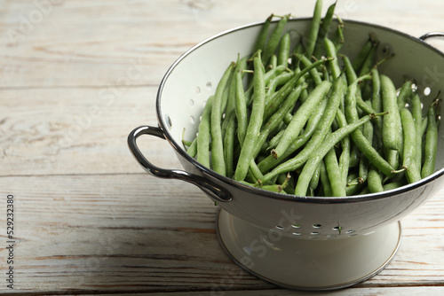 Fresh green beans in colander on white wooden table