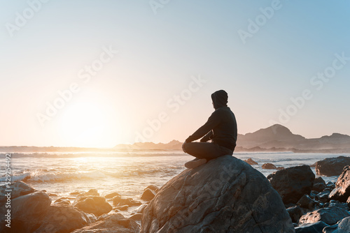 silhouette of a person sitting meditating on the rock on the coast at sunset