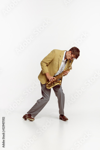 Portrait of young man in stylish yellow jacket playing saxophone isolated over white background. Vintage music