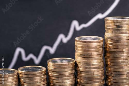 Rising prices and costs due to inflation. Stack of coins in front of a graph with rising curve.