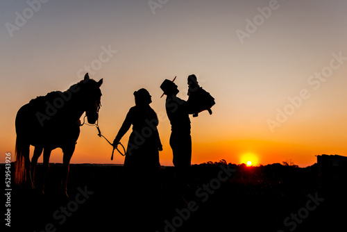 Silhouette of horse and gaucho family at sunset in the countryside.