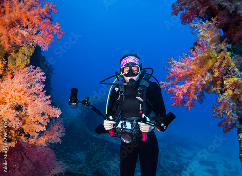 An underwater photographer holding her camera swimming between some beautiful vibrant colored soft coral