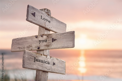 love you jessica written on wooden signpost outdoors on the beach with romatic sunset in the back. Power words and popular name concept.