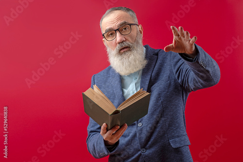 Senior litterateur, man of letters, bookman with a gray beard in a light shirt in a dark casual jacket holding a book