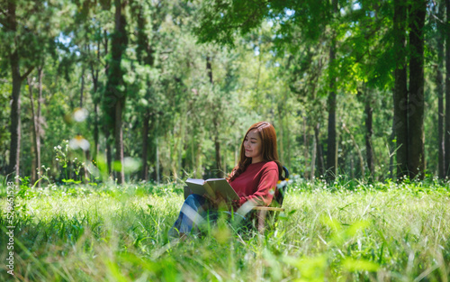Portrait of a beautiful young asian woman reading a book while sitting on a camping chair in the park