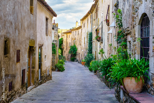 Beautiful alley with old stone houses and pots on the street with plants and flowers, Monells, Girona, Catalonia.