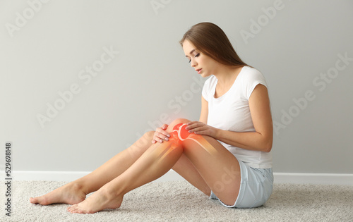 Woman with pain in knee on light background