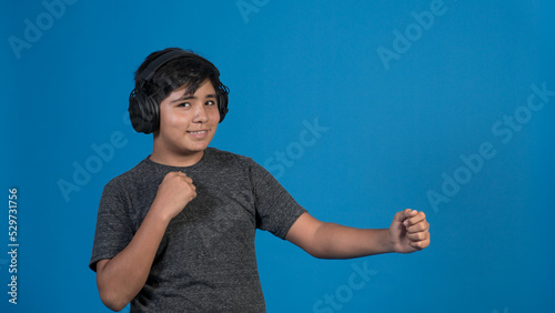 Retrato de estudio de un niño cantando con micrófono y audífonos mientras baila. Con fondo Azul