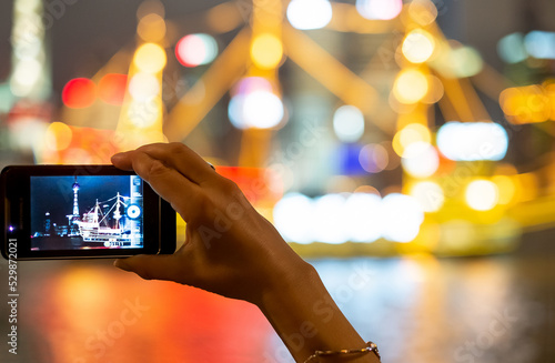 Personne prenant une photo de nuit avec un smartphone, arrière plan lumières colorées