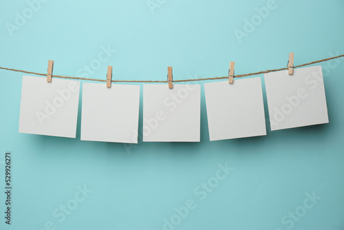 Wooden clothespins with blank notepapers on twine against light blue background. Space for text