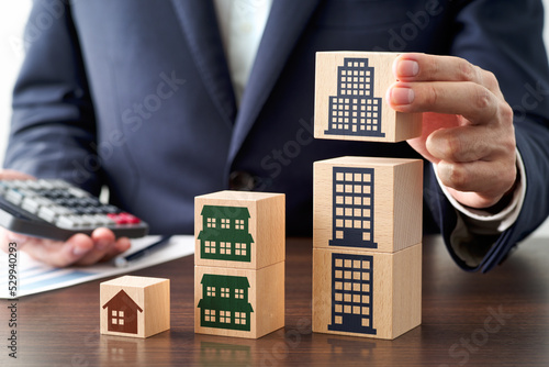 Successful property investment image. Business person calculating rent income and buying property. Stacking wood blocks on table.