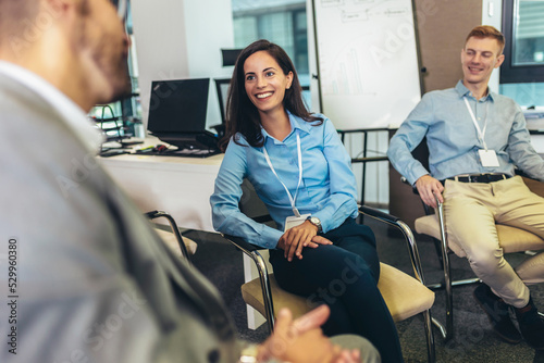 Confident young businesswoman with accreditation badge around her neck talking with colleague at business event