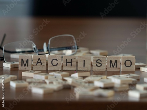 machismo word or concept represented by wooden letter tiles on a wooden table with glasses and a book