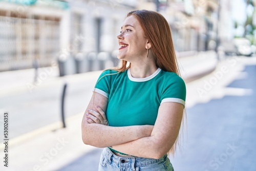 Young redhead woman standing with arms crossed gesture at street