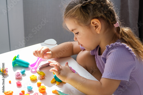 children with plasticine, little blonde girl sculpts various colorful figurines from plasticine at home