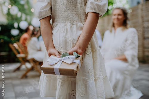 Rear view of little child giving wedding gift to mature bride at wedding backyard party.