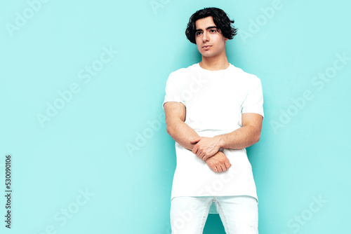 Portrait of handsome confident stylish hipster lambersexual model. Sexy man dressed in over size T-shirt and jeans. Fashion male isolated in studio. Posing near blue wall