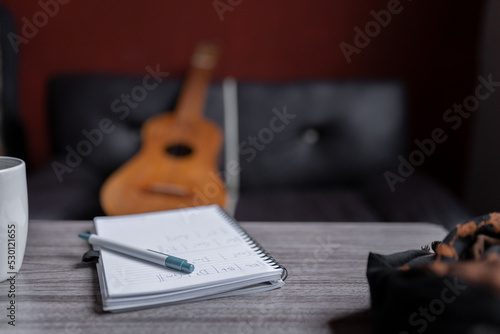 A notebook with music chords is resting on a table with a Mexican jarana guitar in the background