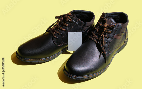 Winter boots with blank tag on yellow background. Pair of leather men's shoes. Male black leather elegant shoe.