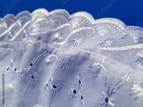 Wavy white lace batiste with a floral print, in the sun, on a blue background