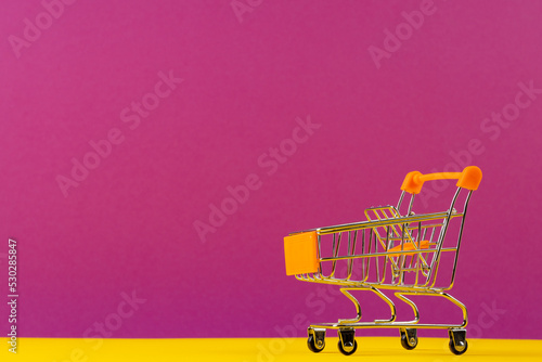 Composition of shopping cart on pink and yellow background