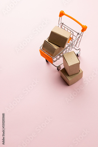 Composition of shopping cart with boxes on pink background
