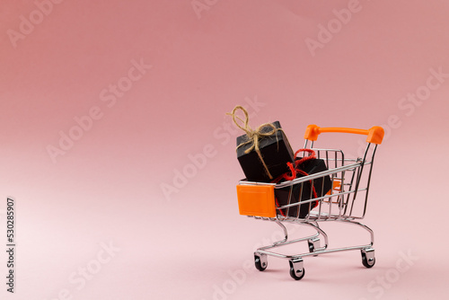 Composition of shopping cart with presents on pink background