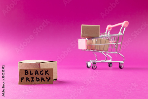 Composition of shopping cart with boxes and black friday text on pink background