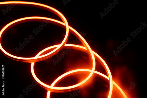 Image of vibrant spiral orange neon glow sticks over black background with copy space