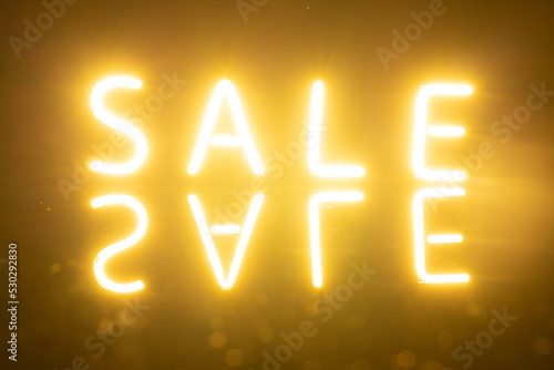 Image of glowing neon sale text with reflection over orange background
