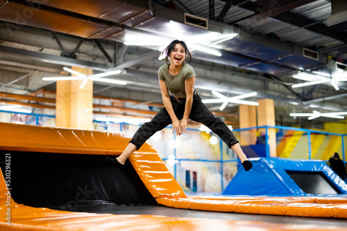 Pretty girl jumping on colorful trampoline at playground park, posing and laughing. Beautiful female teenager happy during active entertaiments indoor