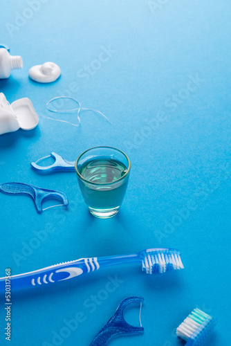 Vertical image of toothbrush, toothpaste, string and liquid on blue surface